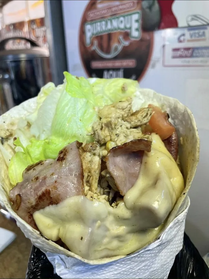 Fajita rellena con pollo, tocino, queso y lechuga, envuelta en papel sobre el mostrador.